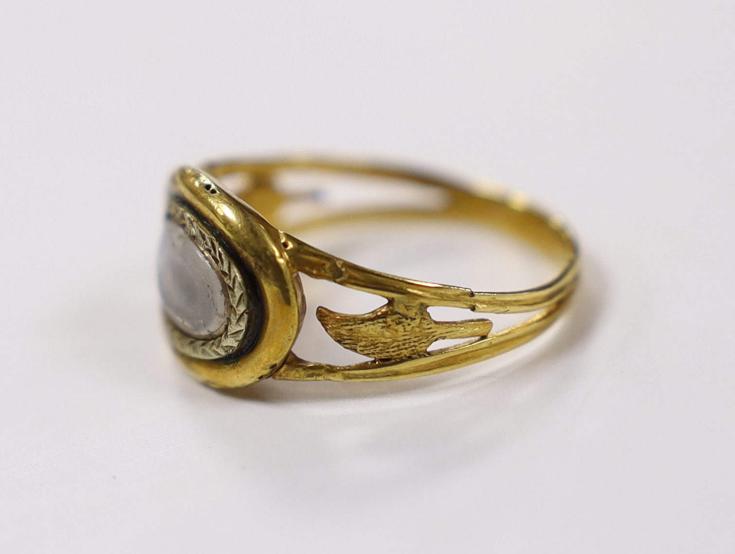 An early 19th century two colour yellow metal mourning ring, with glazed panel and pierced foliate shoulders, size R, gross weight 2.4 grams.